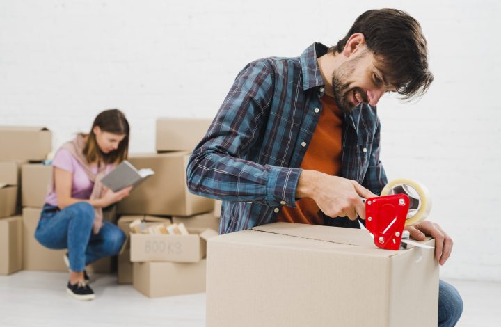 happy-young-man-packing-cardboard-box-her-wife-background